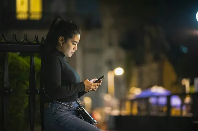 Frau liest abends in der Stadt auf ihrem Smartphone