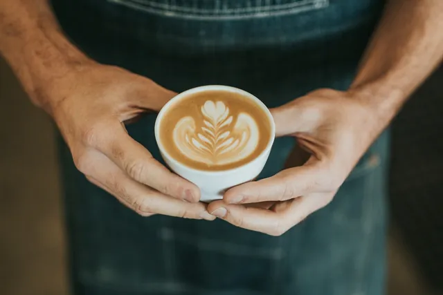 Barista hält einen Cappuccino mit Latte Art in beiden Händen