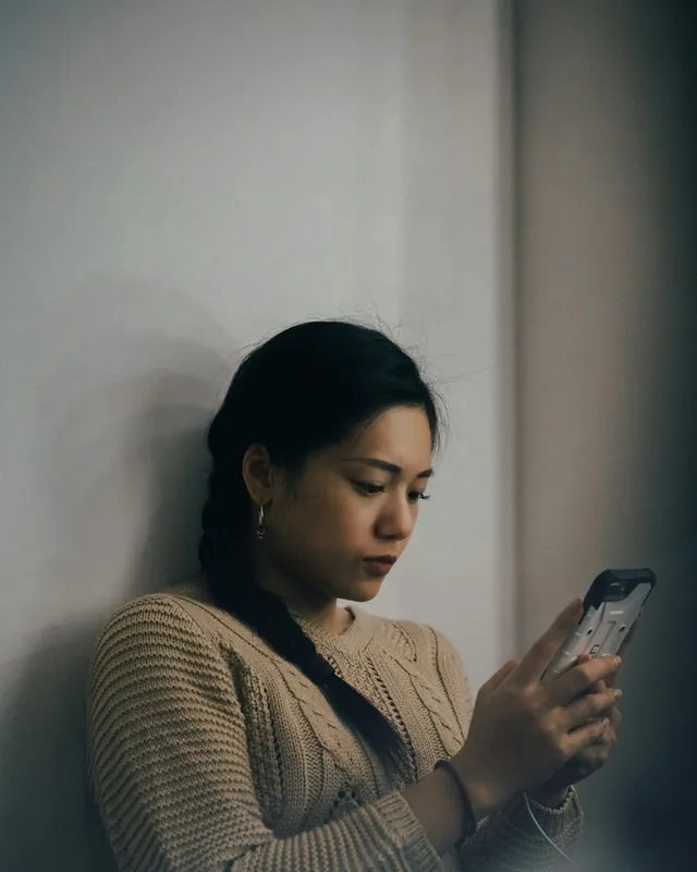 Junge Frau lehnt an einer Wand und liest eine Nachricht auf ihrem Smartphone
