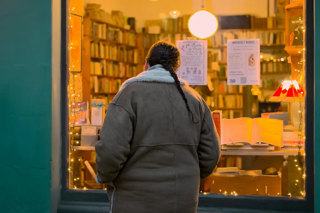 Eine Kundin steht abends vor dem beleuchteten Schaufenster eines kleinen Ladens